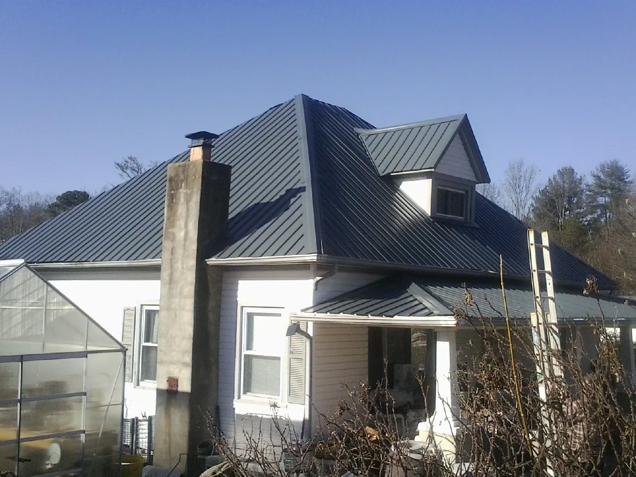 Dark blue standing seam metal roof on a white farmhouse with dormer — Slate & Tile Roof Repair by Roofing Brothers in Hiawatha