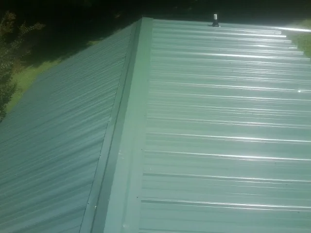 New green metal panels meeting at the ridge of a roof — Flat Roof Repair work by our crew in Hiawatha
