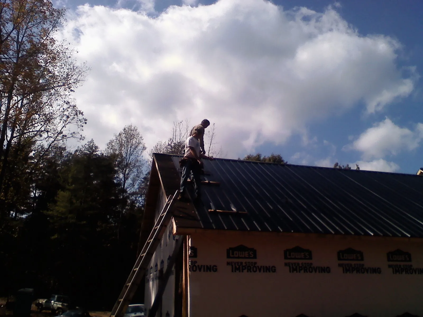 Roofer fastening dark metal panels high against a cloudy sky, from a Roof Inspection job in Hiawatha