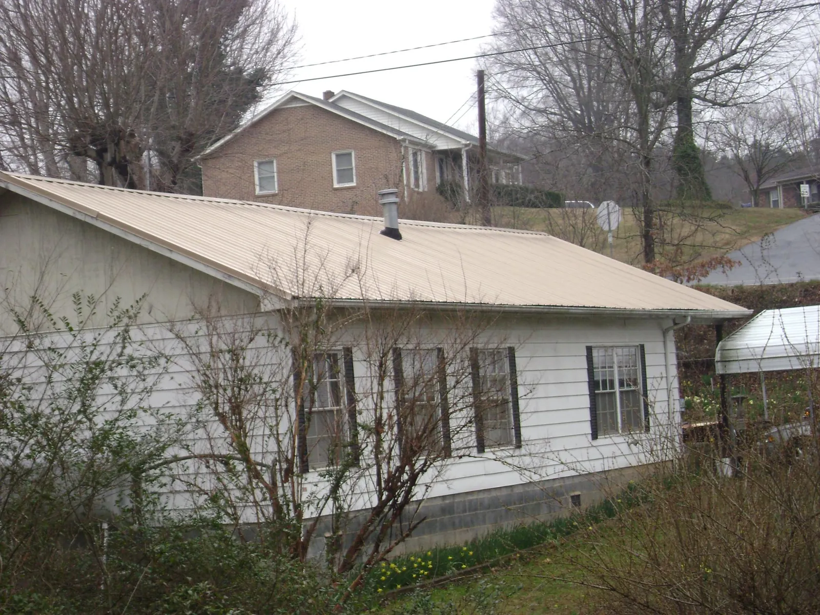 Tan metal roof on a white sided house set into a hillside — Commercial Roofing by Roofing Brothers in Hiawatha