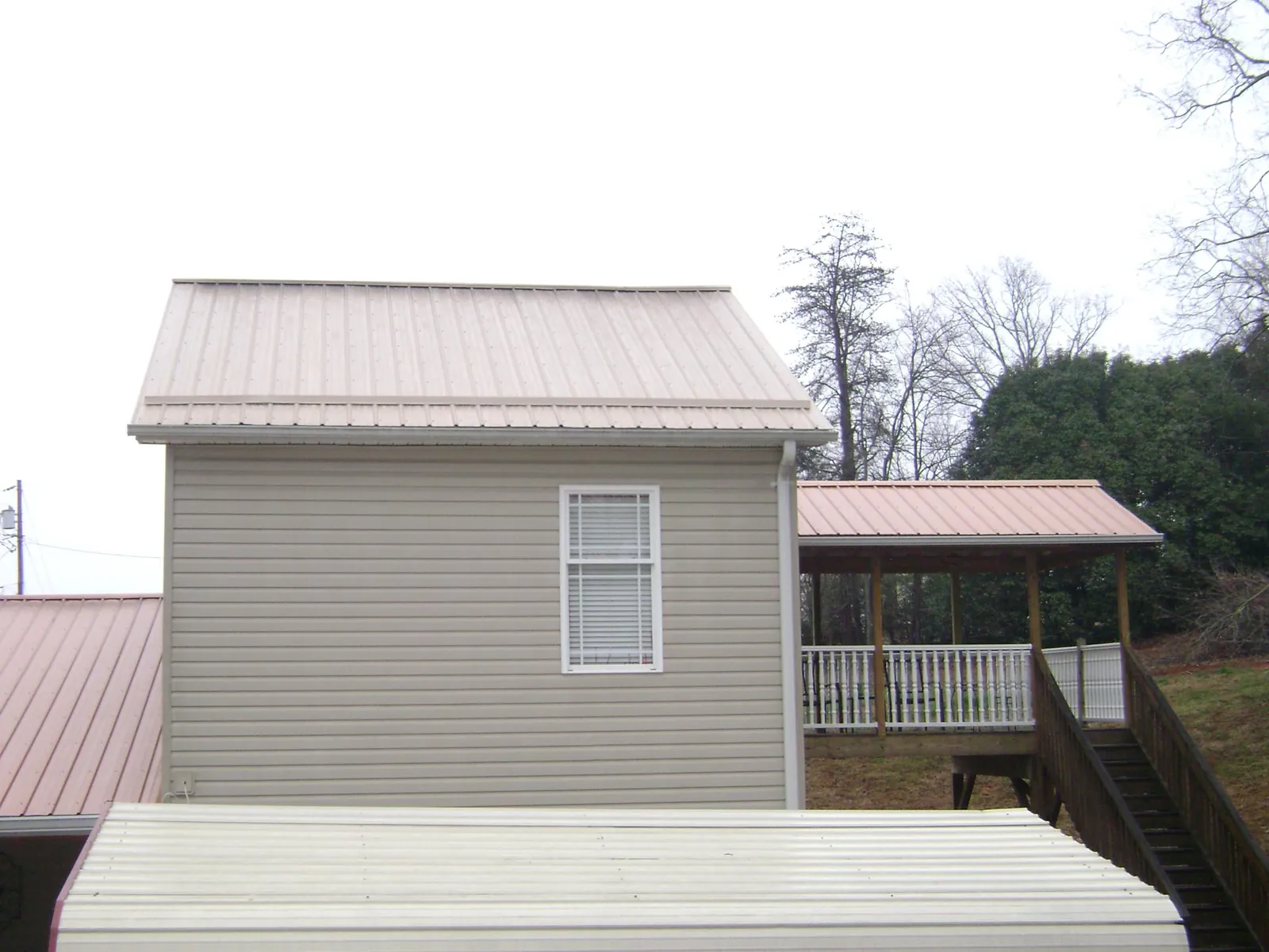 Tan metal roofs on a two story addition and attached porch, from a Roof Replacement job in Hiawatha